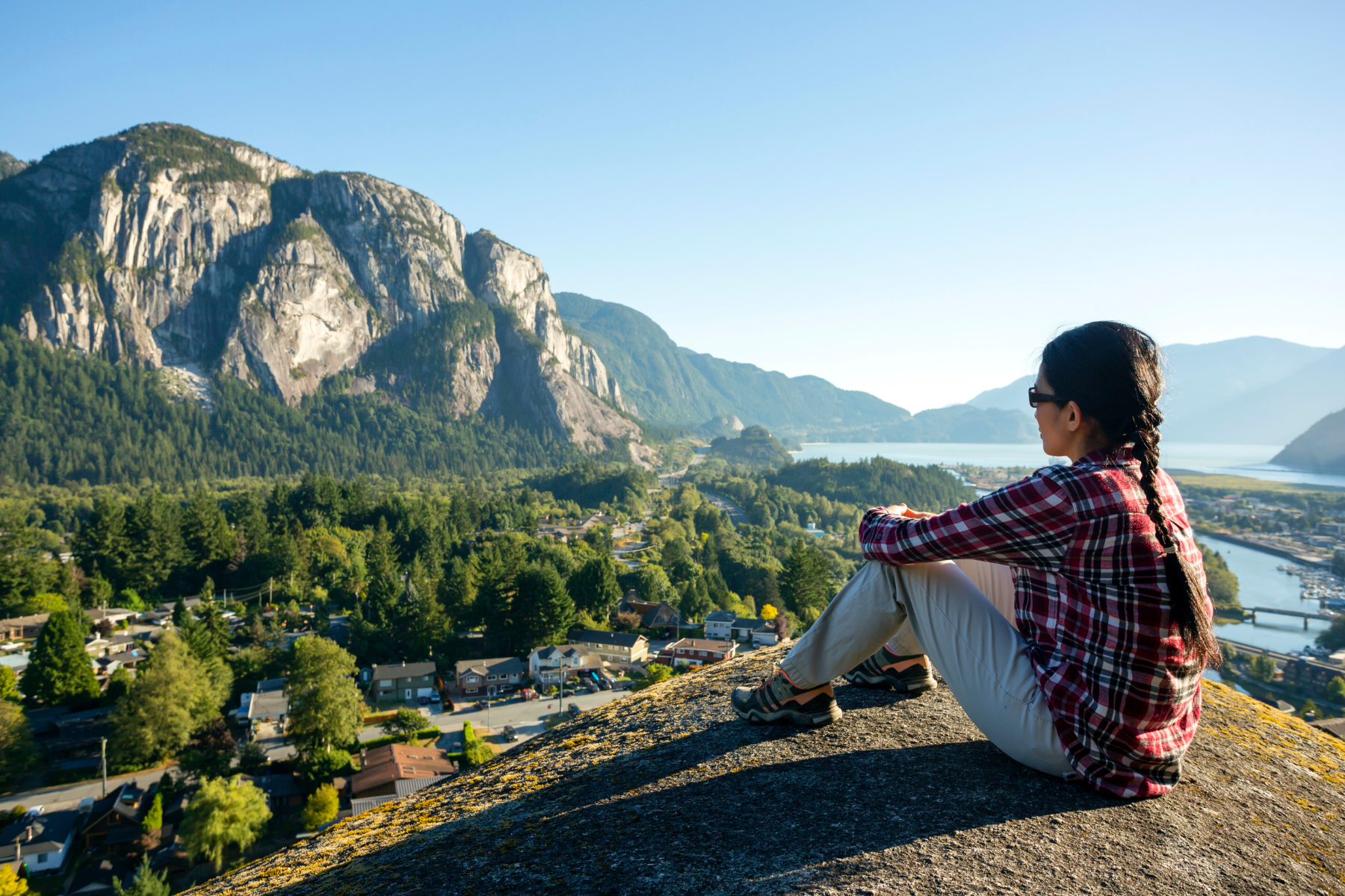 A person sitting on top of a hill looking out over Squamish, the chief is visible in the background