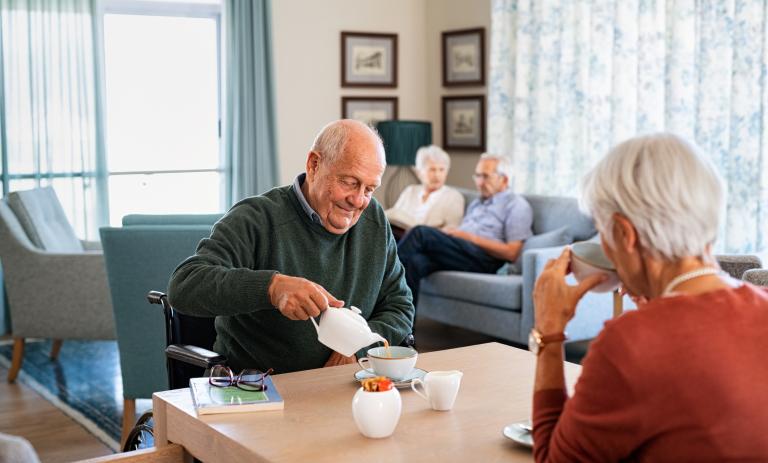 Two seniors have coffee in the common area of a residential care home