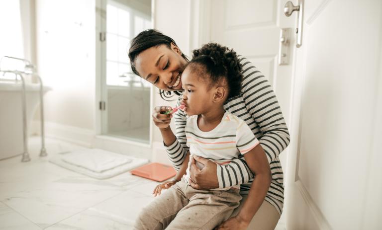 A parent helps their child help their child brush their teeth