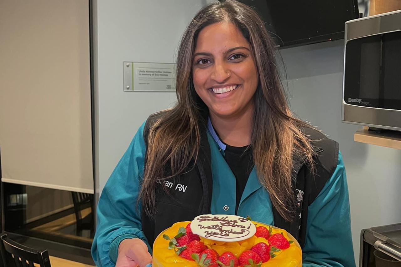 Simran Bir, Specialty Nurse/RN-ICU, standing with a cake in hand.