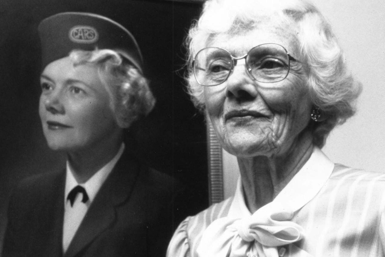 Mary Pack as an older adult standing in front of a photo of herself when she was younger.