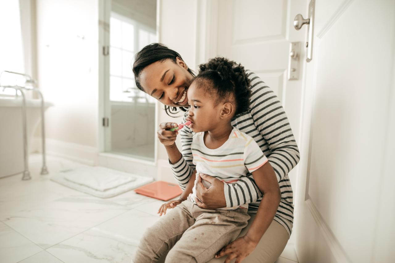 A parent helps their child help their child brush their teeth