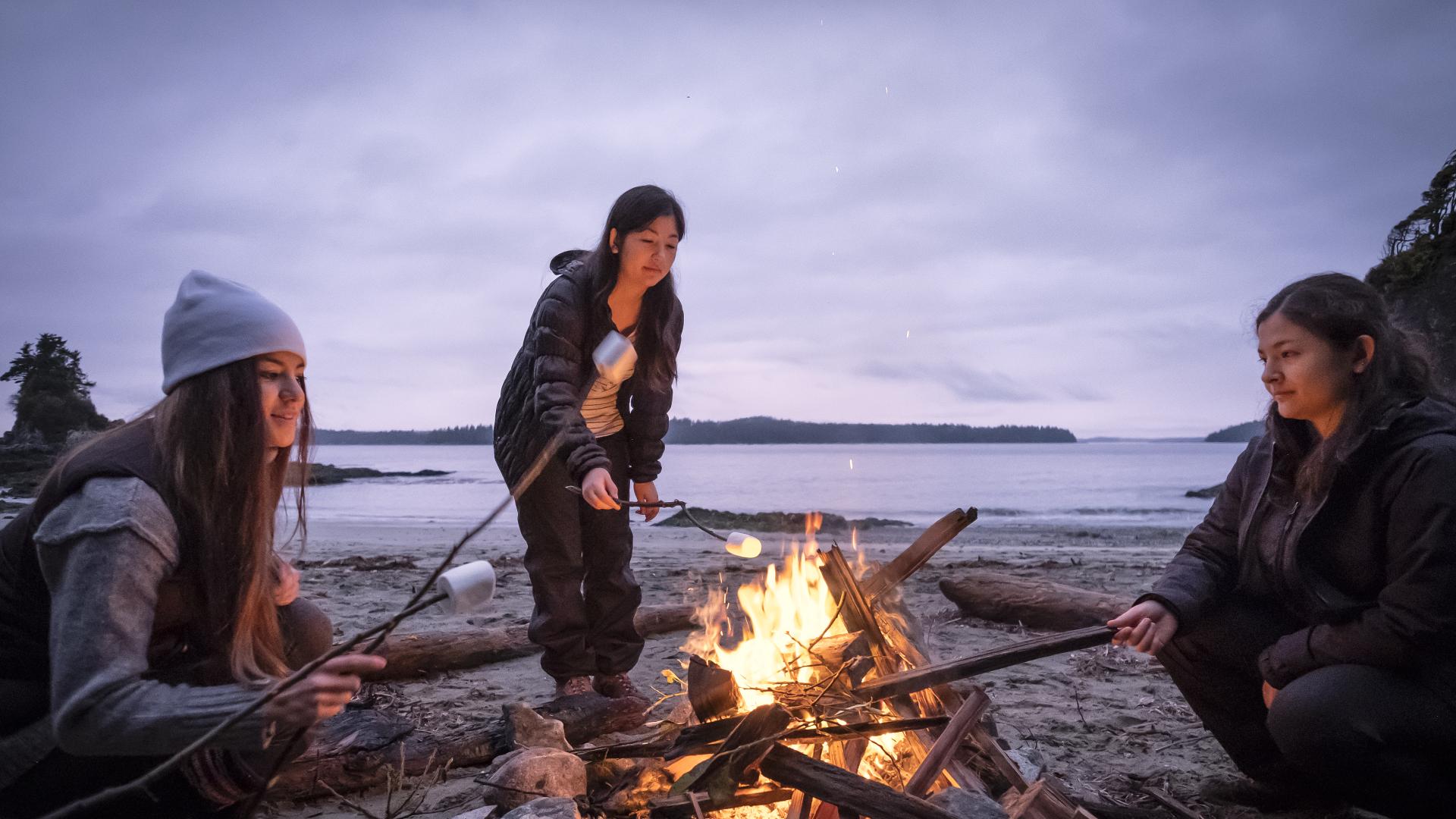 Three females gathered around a fire at the beach