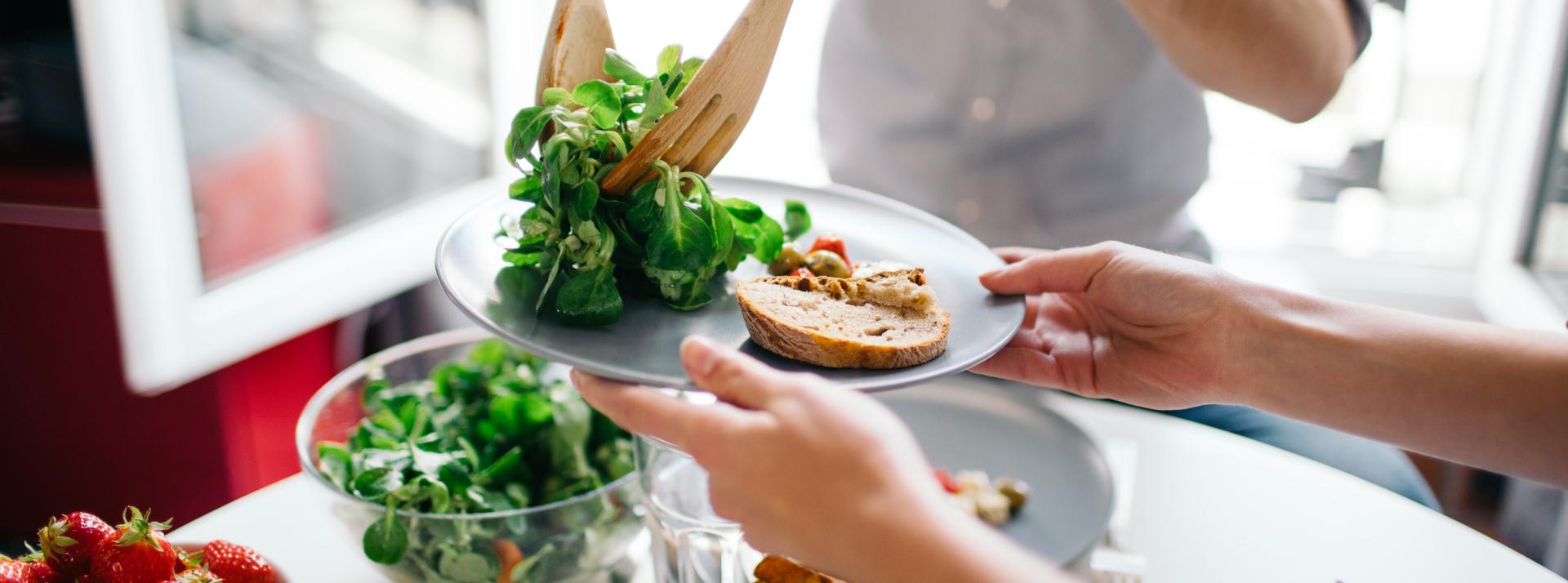 A person serving another salad while having lunch indoors.