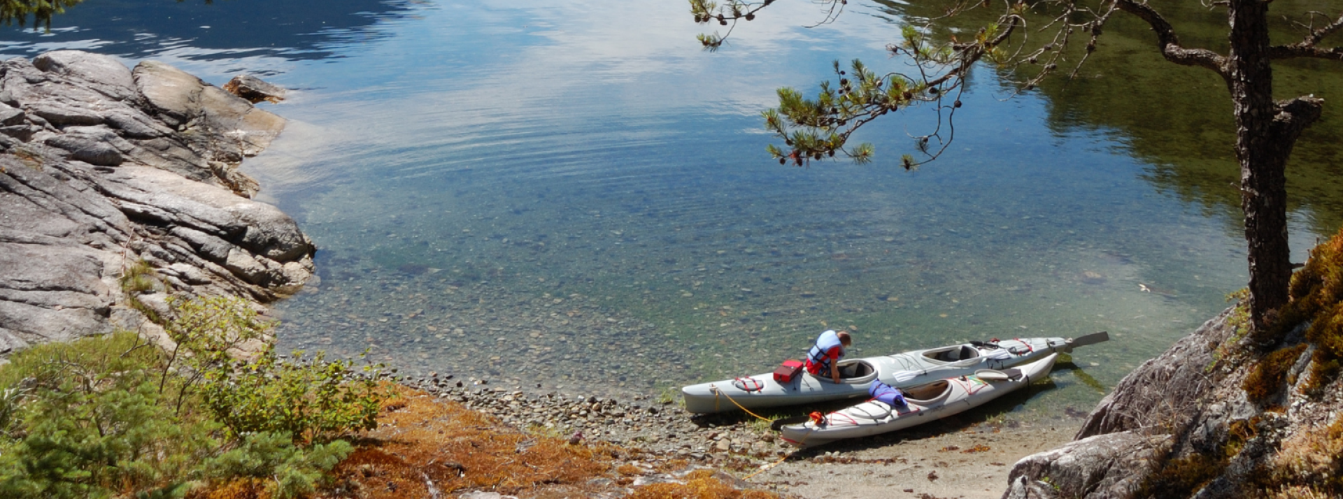 Two kayaks near the shore with one person getting into one of the kayaks.