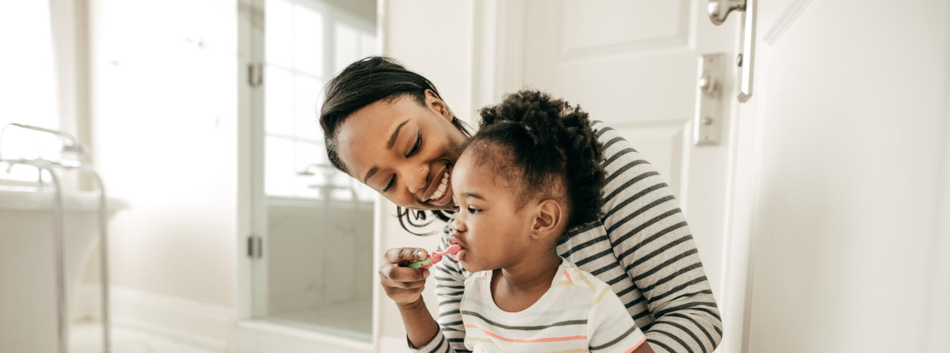 A parent helps their child help their child brush their teeth