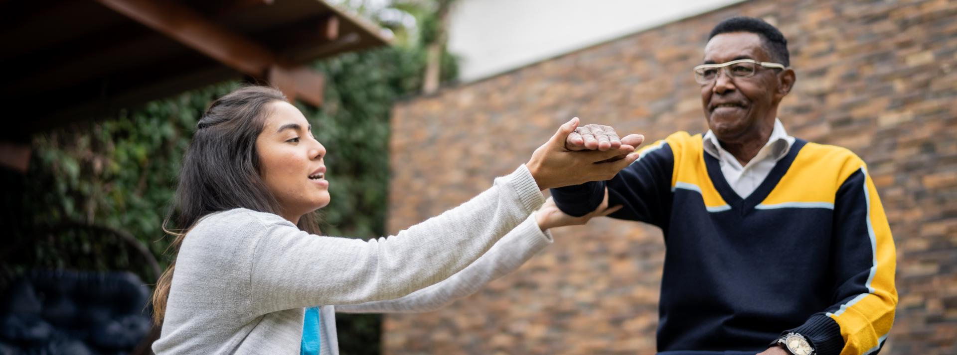 A physiotherapist helps an older person with rehab excercises outdoors.