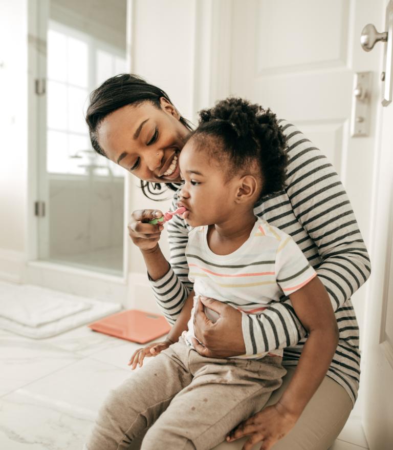 A parent helps their child help their child brush their teeth