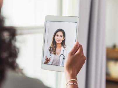 Person's hand holding a tablet with a medical professional on the screen.