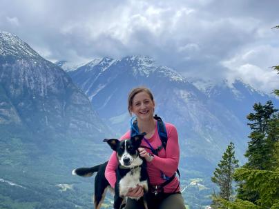 Brooke Meunier, LPN, crouched on a cliff with a dog in arm.